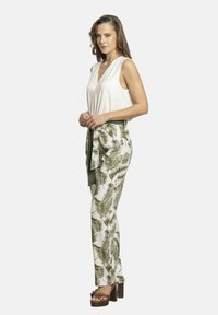 Top blanco sin mangas combinado con pantalones verdes y blancos con un diseño de hojas y un cinturón de tela verde. Sandalias marrones de tacón.