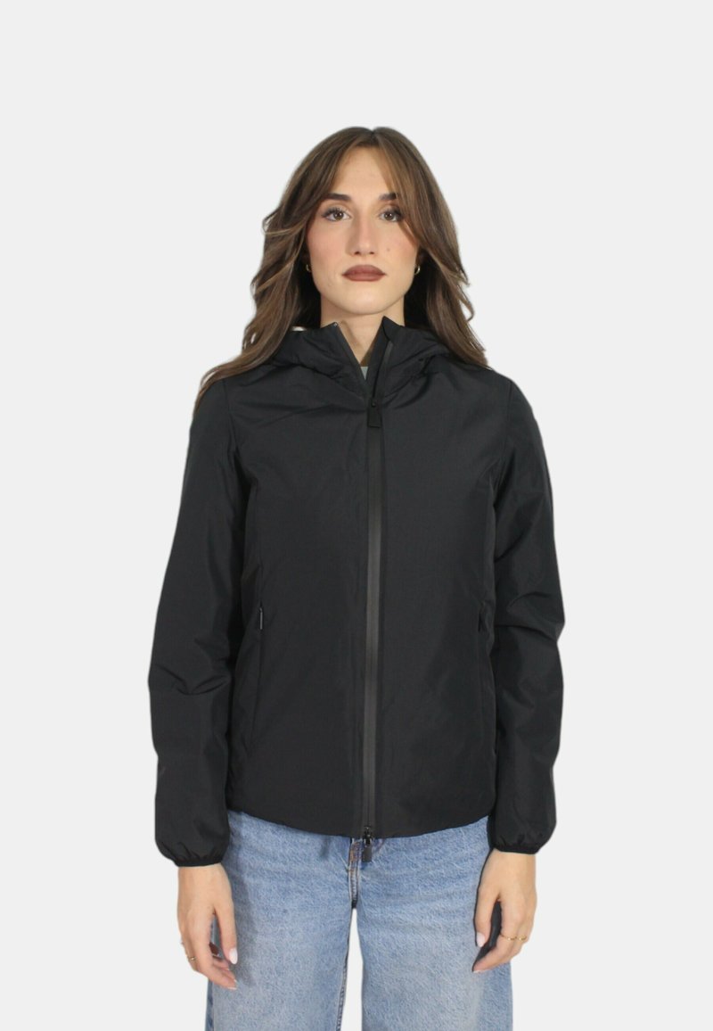 Giacca leggera nera con zip frontale, cappuccio e polsini elastici. Presenta una texture liscia e due tasche laterali, indossata su jeans blu.