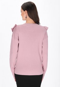 Jasnoróżowy sweter z prążkowanej dzianiny, z krótkimi rękawami, z falbaniastymi akcentami na ramionach i okrągłym dekoltem.