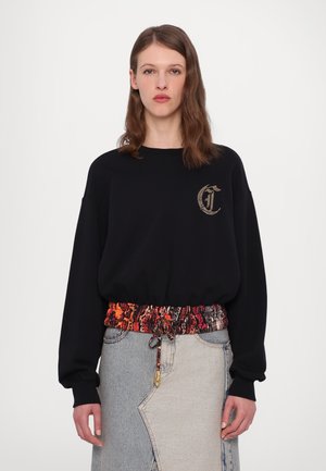 Sweatshirt noir à manches longues avec une taille froncée à motif multicolore. Présente un logo doré sur la poitrine et une jupe en denim clair.