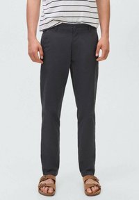 Mörkgrå byxor i lättviktsmaterial; slim fit-design med knäppning; bärs med en randig skjorta och bruna sandaler.