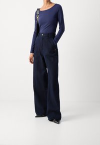 Mörkblå långärmad topp i kombination med hög midja och vida denimbyxor. Byxorna har en knappstängning och två sidofickor. Svarta skodon med spetsig tå.