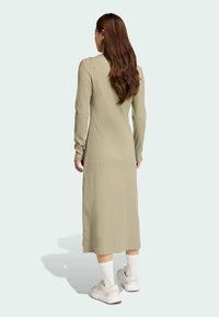 Lichte olijfgroene ribben midi-jurk met lange mouwen. Heeft een getailleerde pasvorm en een ronde hals, gecombineerd met witte sneakers.