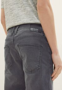 Jeans in denim grigio con una vestibilità elegante, caratterizzati da tasche posteriori distintive e un'etichetta nera con la scritta "IDENIM TOM TAILOR" in vita.