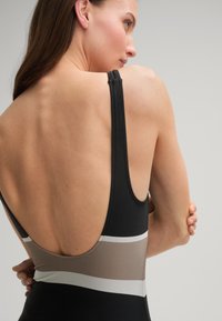Maillot de bain une pièce noir avec des rayures horizontales beige et argent. Présente un dos profond et de fines bretelles. Texture de tissu lisse.