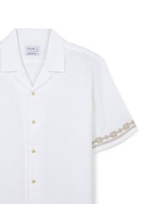 Camisetta bianca a maniche corte con una vestibilità comoda. Presenta motivi geometrici ricamati color sabbia sulle maniche. Colletto arrotondato con chiusura a bottone.