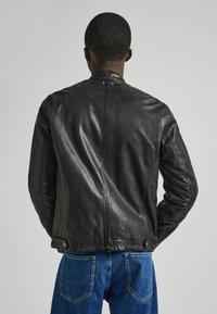 Giubbotto di pelle nera con una texture liscia, caratterizzato da un colletto alto e tasche laterali. Il design è elegante, con dettagli minimi.