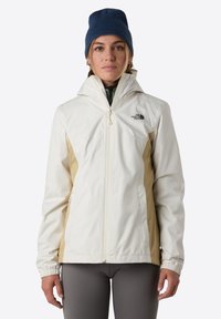 Vit och beige huva jacka med dragkedja fram, elastiska ärmar, och The North Face-logotyp på vänster bröst. Bärs över ett grönt plagg.