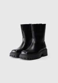 Mustad mustad käised mustadest nahast, pakse ja robustse taldaga, millel on sügavad tallakäigud, tõmbeloogid ja ümar varvas.