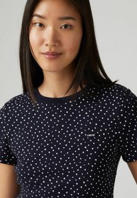 Marineblaue T-Shirt mit weißen Punkten, kurzen Ärmeln, rundem Halsausschnitt, mit einem kleinen schwarzen Levi's-Logo auf der linken Brust.