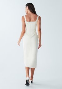 Robe ajustée de couleur crème avec un décolleté carré, des bretelles fines et une longueur mi-mollet. Dispose d'une fermeture éclair et d'une texture de tissu lisse.