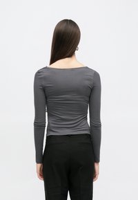 Γκρι μακρυμάνικη εφαρμοστή μπλούζα με φαρδιά λαιμόκοψη και διακριτικές πιέτες στους ώμους, συνδυασμένη με μαύρο, ραμμένο κατά παραγγελία παντελόνι.