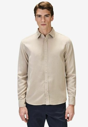 Beige napapaita, jossa on klassinen kaulus ja pitkät hihat, sujuvalla pinnalla ja suoran helmalla. Yhdistetty tummiin housuihin.