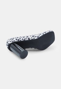 Čevlji z visokim petami z zgornjim delom iz črno-belega leopardjega vzorca, sijočim črnim cilindričnim petami in teksturiranim črnim podplatom.