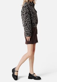 Kraťoučká, huňatá bunda s leopardím vzorem v šedé a hnědé barvě, doplněná o hnědou mini sukni a černé Mary Jane boty na platformě.
