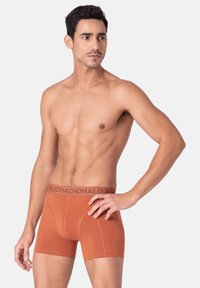 Oranžni bokserice iz mehke tkanine z oprijetim dizajnom. Pas ima temno rjavo logotipno elastiko. Brez opaznih vzorcev ali dodatkov.