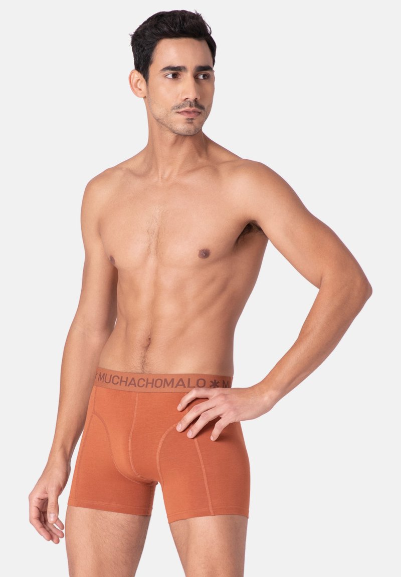 Oranžni bokserice iz mehke tkanine z oprijetim dizajnom. Pas ima temno rjavo logotipno elastiko. Brez opaznih vzorcev ali dodatkov.