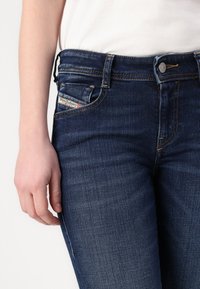Dunkelblaue Jeans aus Denim mit taillierter Passform, ausgestattet mit gelben Nähten, einem Metallknopfverschluss und einem kleinen Label auf der Vorderseite der Tasche.