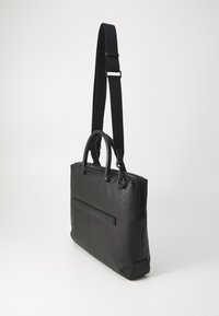 Serviette en cuir noir avec une finition texturée. Elle comporte deux poignées et une bandoulière amovible et réglable. Fermeture éclair et poche arrière.