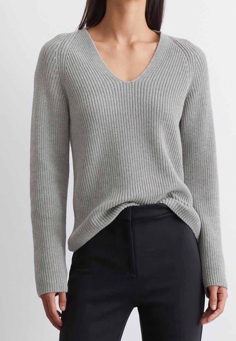 Maglione grigio lavorato a maglia con scollo a V, texture a coste e maniche lunghe. Abbinato a pantaloni neri, che mostrano una vestibilità comoda e cuciture minime.