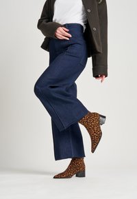 Pantalones de mezclilla oscuros de pierna ancha combinados con botines de punta de print de leopardo, que cuentan con un bajo tacón cuadrado y una tela texturizada.