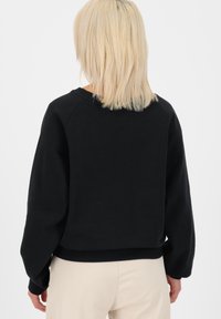 Musta huppari rennolla leikkauksella, joustavat hihansuut ja pyöreä kaula-aukko. Pehmeä materiaali ja sileä pinta ilman näkyviä kuvioita.