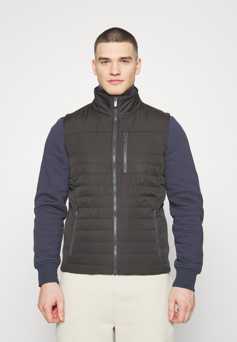 Černá vatovaná vesta s vysokým límcem, předním zipem a bočními kapsami, s prošívanými detaily a hladkou texturou látky.