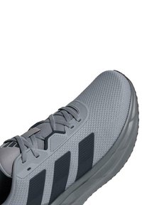 Scarpa sportiva grigia con tomaia in mesh testurizzato, tre strisce scure di lato e suola ammortizzata per il comfort.