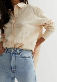 Ljust beige knäppskjorta med krage, med en strukturerad tyg och enkelknäppte ärmar, kombinerad med ljusblå denimjeans.