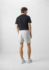 T-shirt noir à manches courtes et short gris clair. Le short est équipé d'une taille élastique avec cordon de serrage, de poches latérales et est légèrement plus long.