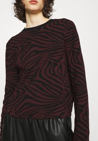 Burgundský svetr s černým pruhovaným vzorem zebry, kulatým výstřihem a dlouhými rukávy. Kombinováno s černou skládací koženou sukní.