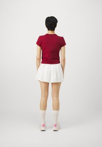 Punane lühikeste varrukatega keha järgi istuv topp valge voltidega mini seelikuga. Valged põlvikud ja roosad tennised täiendavad rõivastust.