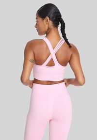 Różowy sportowy stanik z krzyżującymi się ramiączkami, teksturowana tkanina i dopasowany krój, w zestawie z pasującymi legginsami o wysokim stanie.