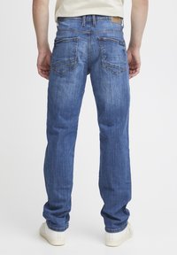 Jeans de mezclilla azul con corte recto, costuras visibles en los bolsillos traseros y una etiqueta de marca de cuero en la cinturilla.