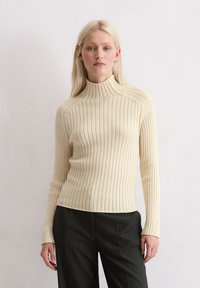 Crème ribgebreide coltrui met lange mouwen en een aansluitende pasvorm, met een gladde textuur en een licht cropped zoom.