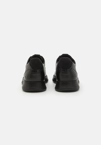 Black athletic shoes with a smooth leather finish, rounded toe, and cushioned heel. Features a low profile and a minimalistic design.