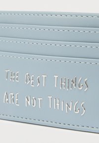 Světlomodrá kožená peněženka s prošívaným stříbrným textem "NEJLEPŠÍ VĚCI NEJSOU VĚCI." Má šest přihrádek na karty a bílé prošití.