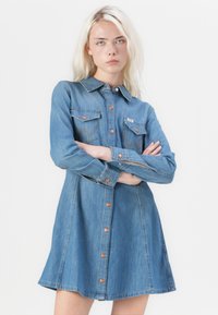Denim dress with long sleeves, button closure, two chest pockets, and a flared skirt. Made of light blue denim with a subtle texture.