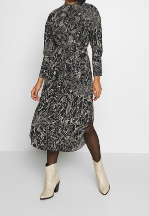 Zwarte midi-jurk met witte bloemenprint, lange mouwen, hoge kraag, getailleerde taille, split aan de zijkant, gecombineerd met gestructureerde beige enkelboots.