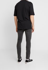 Svart bomullströja med korta ärmar, matchad med grå denimjeans och svarta Vans-skor. Outfiten har en avslappnad passform och enkel design.