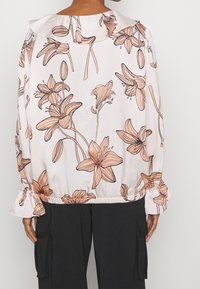 Blusa a maniche lunghe in tessuto morbido, con un motivo floreale in pesca e beige su uno sfondo chiaro, caratterizzata da polsini e vita con volants.