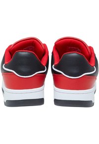 Sorte og røde sneakers med overdel i teksturert skinn, polstret krage og hvit såle. Designet har kontrasterende røde detaljer og sømmer.