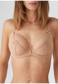 Jasnobeżowy stanik z fiszbinami, siateczkowym wzorem i cienkimi ramiączkami. Posiada subtelne złote okucia oraz strukturalny kształt zapewniający wsparcie.