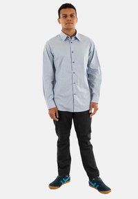 Camisa de botones azul con pequeños lunares negros, combinada con jeans oscuros y zapatillas azules con acentos en negro y turquesa.