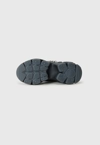 Sort gummisko sål med et tekstureret mønster, der har fremtrædende grip-lugs og en rund form. Holdbart materiale designet til trækkraft.