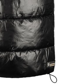 Section de tissu matelassé noir brillant d'une veste avec un patch de marque Sublevel cousu et une boucle de cordon réglable en bas.