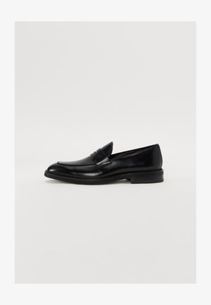 Musta nahkainen loafer, jossa on pyöristetty kärki, huomaamaton ompelu ja sileä pinta. Varustettu matalalla pinnoitetulla korkokengällä ja nauhalla vampin yli.