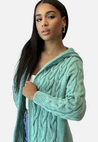 Hellblauer, kabelgestrickter Cardigan mit Kapuze, verziert mit strukturierten Mustern, gerippten Bündchen und offenem Vorderteil. Weiches Material.