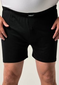 Pantaloni corti neri in cotone con vita elastica e chiusura a un solo bottone, dotati di un'etichetta con la dicitura "MEN+" sulla vita.