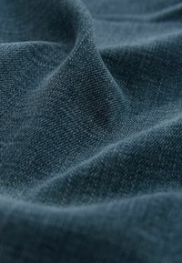 Tissu en denim bleu foncé avec une surface texturée, présentant une apparence douce et légèrement froissée, ainsi que de subtils motifs de tissage.